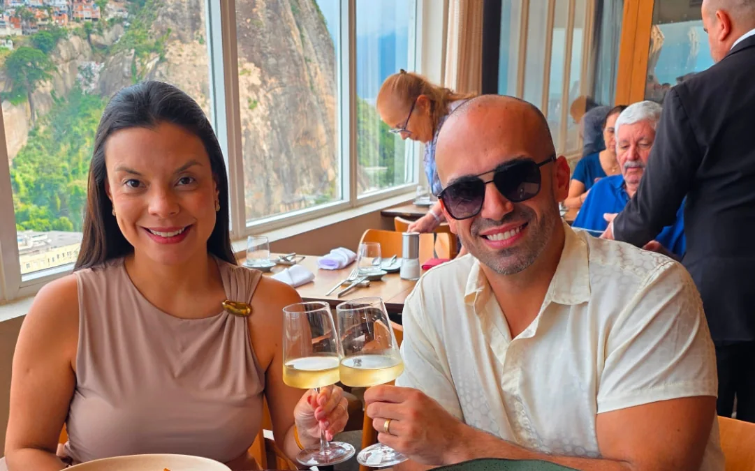 Casal brindando com vinho branco em almoço com vista para o morro e o mar no Rio de Janeiro