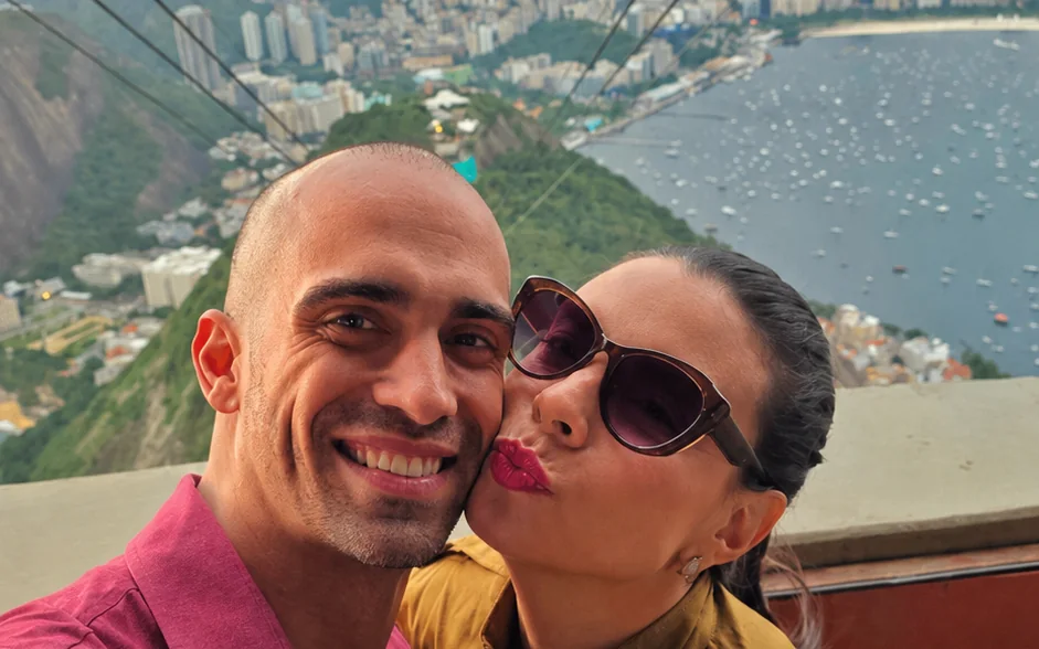Casal no bondinho do Pão de Açúcar com a enseada de Botafogo e a cidade ao fundo